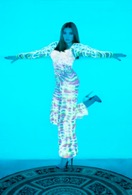 photo of a woman standing on one leg, the other kicked out behind her, against a bright blue background