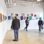 three people in a gallery space looking at artwork on a wall.