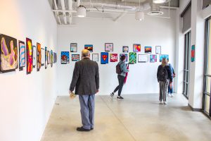 three people in a gallery space looking at artwork on a wall.