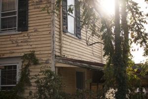 A yellow house covered in ivy with the sun peaking around the corner.