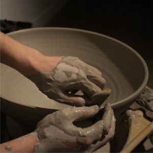 Hands covered in clay spinning a pottery bowl.