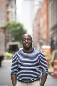 Image of Jerome Harris from the waist up in a stiped shirt, on a city street