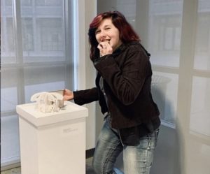 The artist in a dark jacket standing next one of her carousel books on a pedestal.