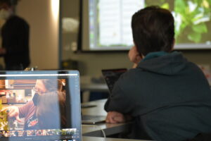 Photograph of an open laptop next to a person facing forwards.