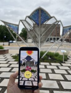 Photo of a hand holding a phone with an augmented reality view of the scene beyond it.